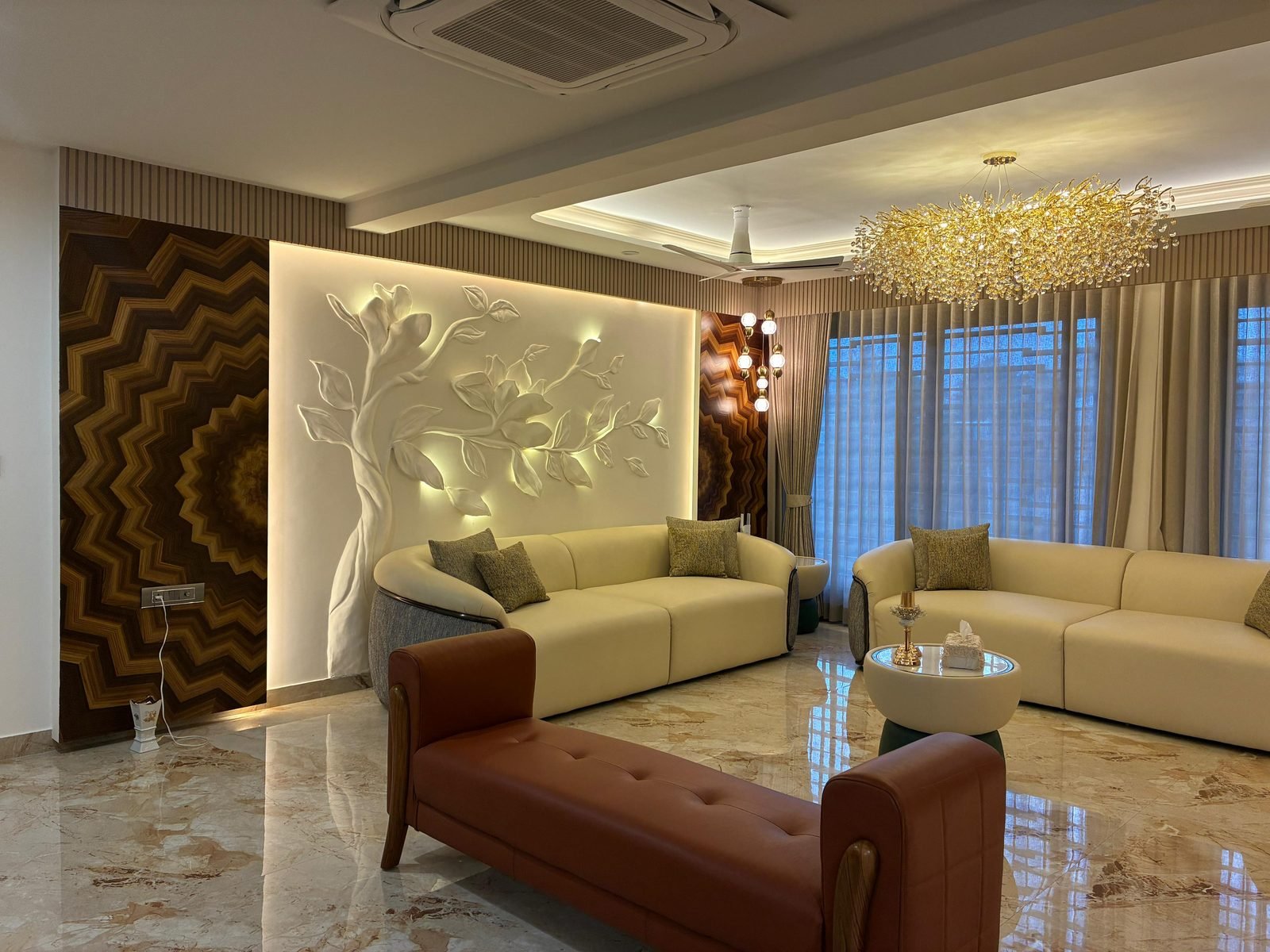 Living room with a carved relief wall, crystal chandelier and cream sofas